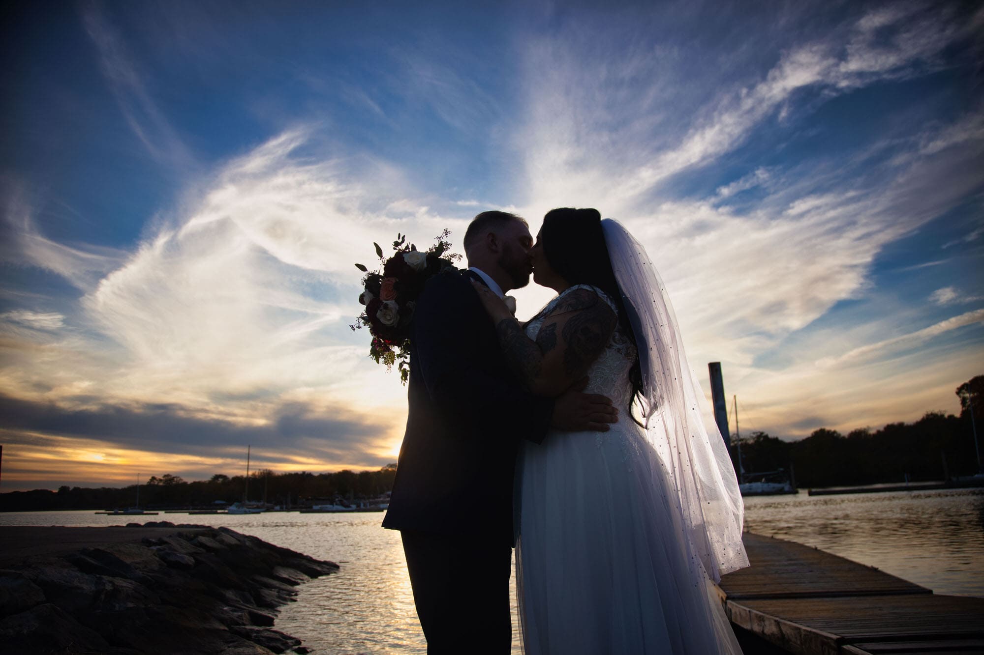 Plus-size-bride-and-groom-in-silhouette-kissing-front-of-epic-sunset