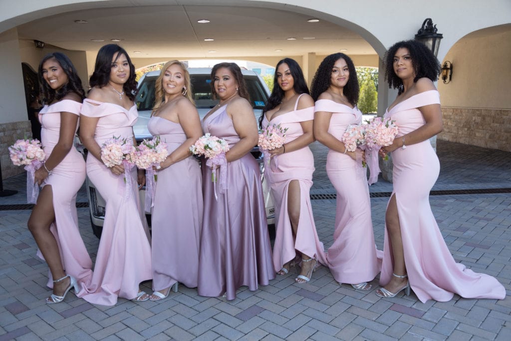 bridesmaids in dusty rose bridesmaid dresses posing front of Cadillac Escalade Limo