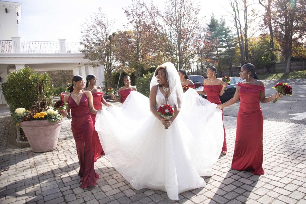 black bridesmaids wearing red brides maid dresses while holding the bride's dress