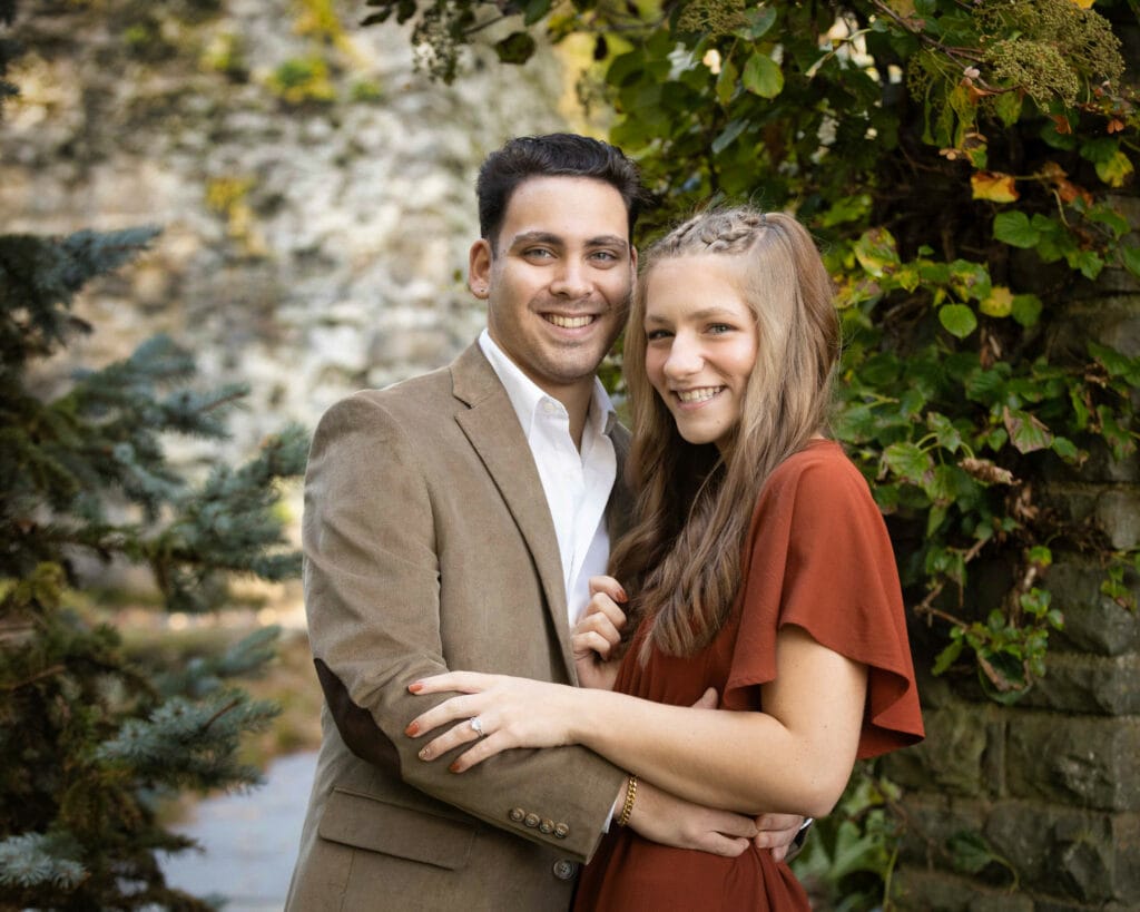 Caucasian engaged couple posing in front of vineyard at Grey Towers in fall foliage