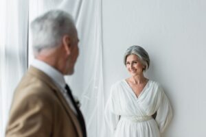 Blurred,Man,In,Suit,Looking,At,Cheerful,Mature,Bride,In