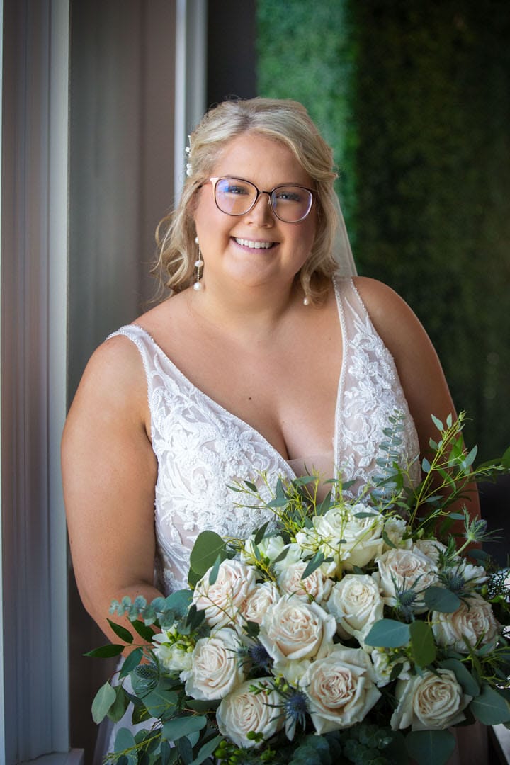 Plus-size Bride smiling and standing in front well-lit soft window light of the The Banks - A Waterfront Venue - Wedding Veune