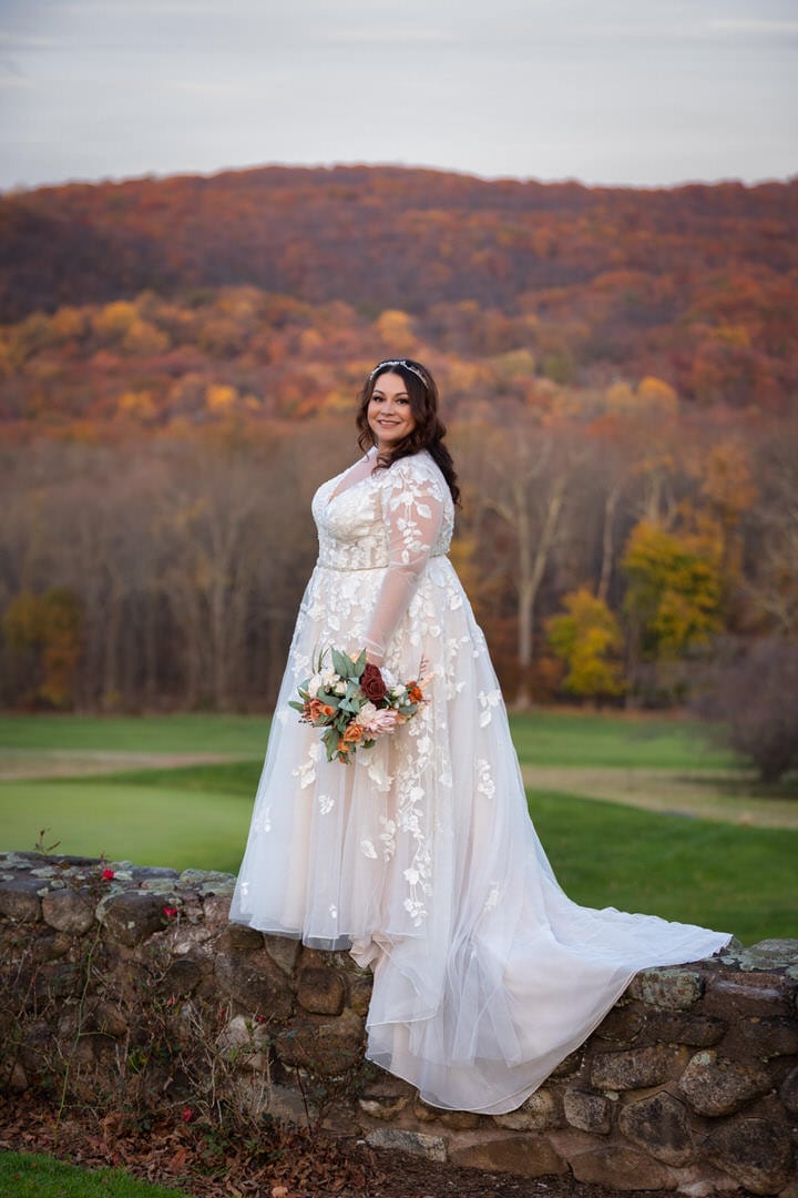 Plus-size bride standing on a Stone wall in front changing autumn leaves